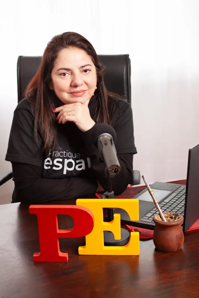 Julia Inés Oscar no escritório do Pratique Espanhol, microfone e logotipo “PE” sobre a mesa